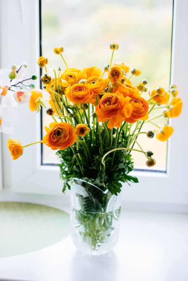 photo of yellow flowers in a glass vase next to a window